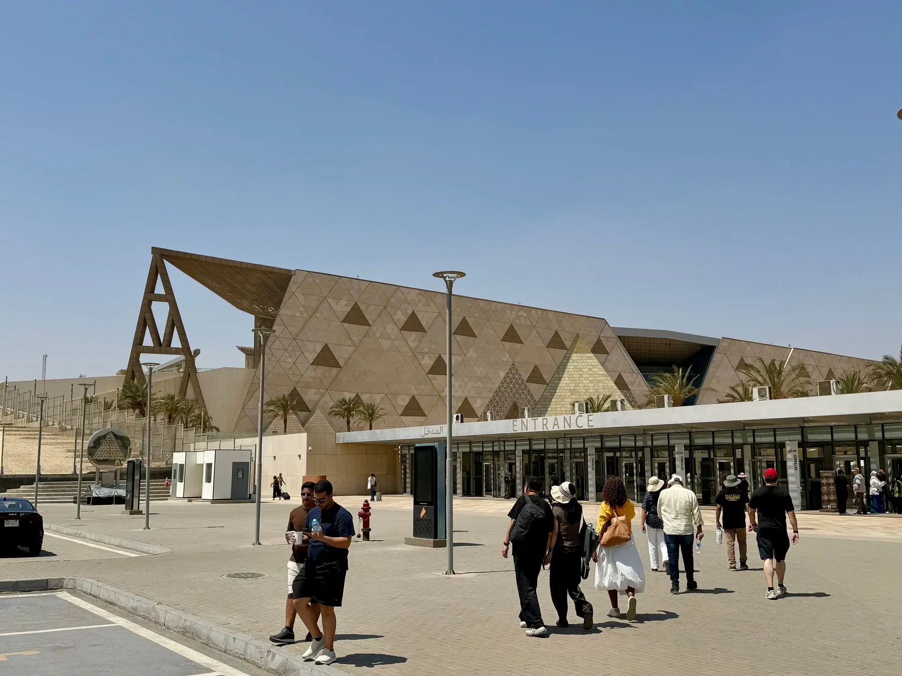 Visitors walking to the entrance of the Grand Egyptian Museum under its triangular stone facade