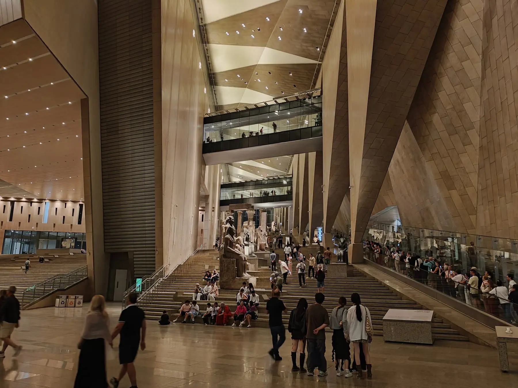 Visitors on the Grand Staircase of the Grand Egyptian Museum, lined with ancient statues
